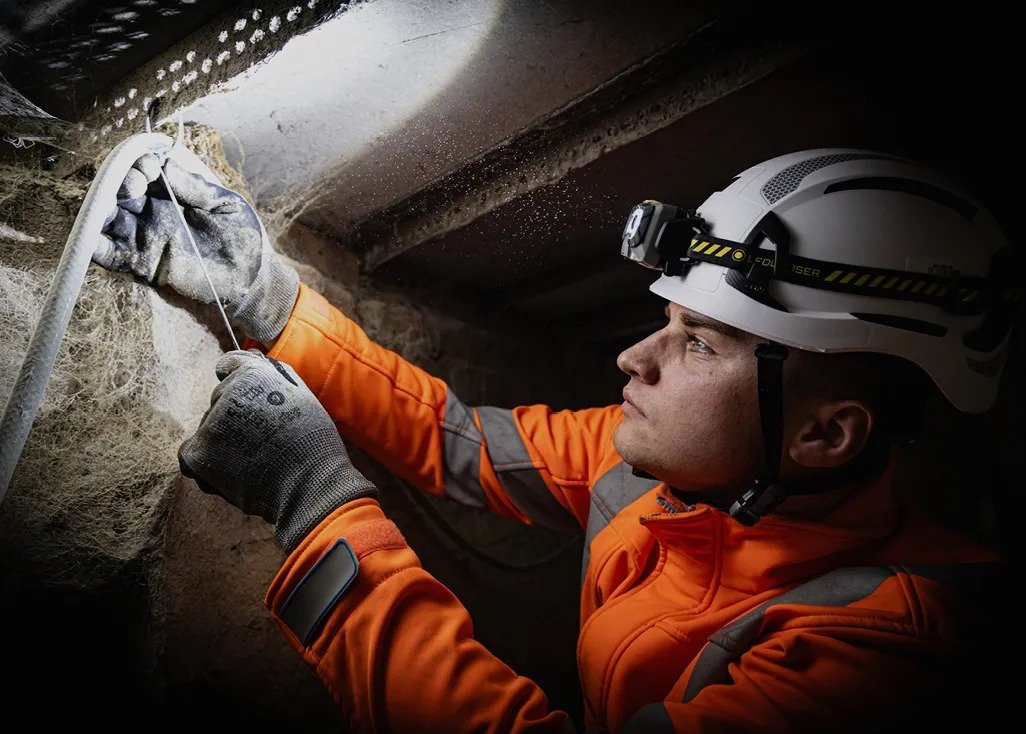 Electrician wearing a Ledlenser head torch pulling cable in a ceiling void
